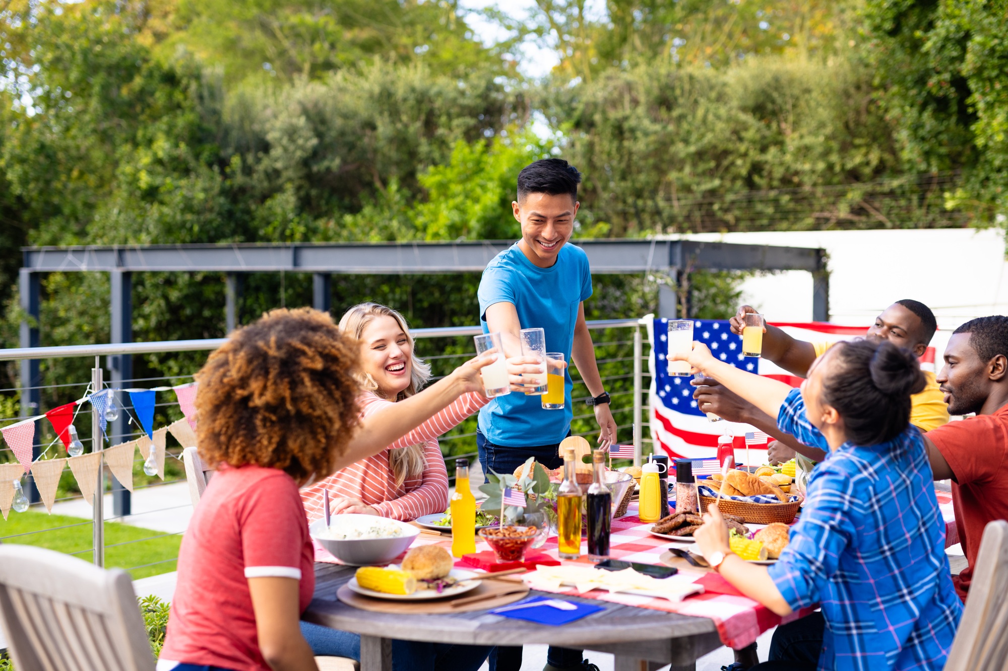 Happy diverse group of friends cheering with drinks and having dinner with flags of usa Happy diverse group of friends cheering with drinks and having dinner with flags of usa