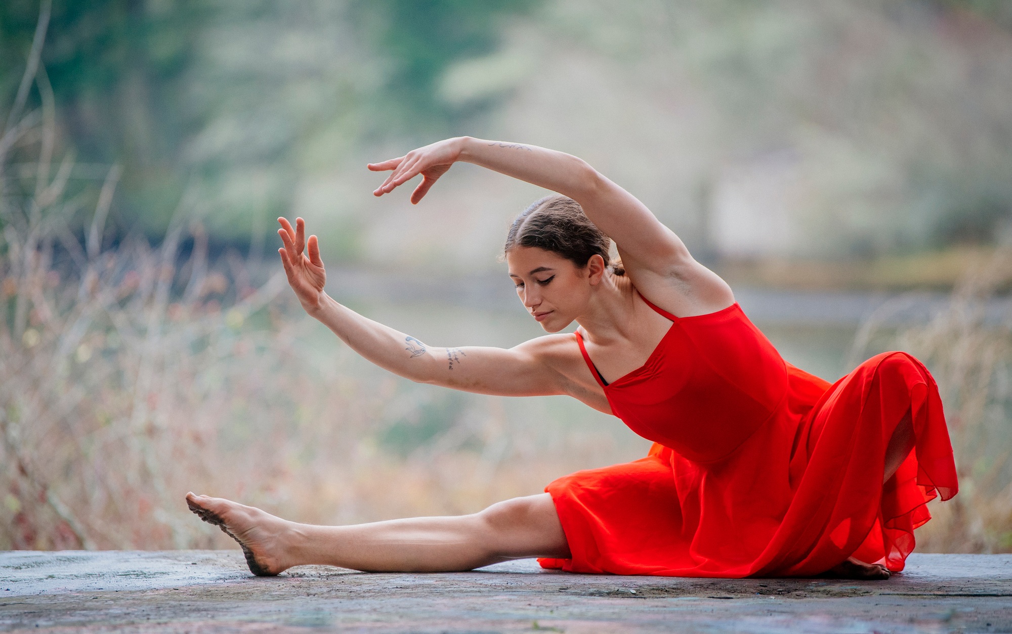 Woman in a red dress gracefully poses in a dance position outdoors. USA
